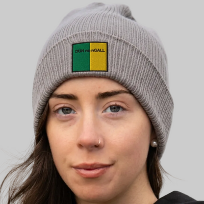 A woman wearing a gray knit beanie with a square patch that reads “DÙN NA NGALL” in black text over green and yellow sections. 