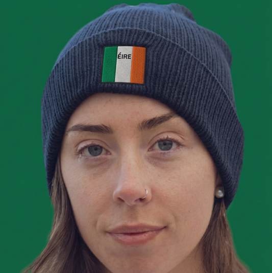 A woman wearing a navy blue ribbed knit beanie with a small Irish flag patch on the front, set against a solid green background.
