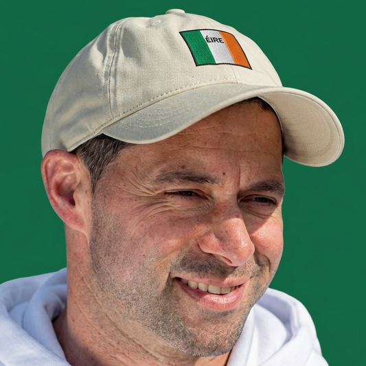 A man wearing a light beige baseball cap with a small Irish flag patch on the front, set against a solid green background.