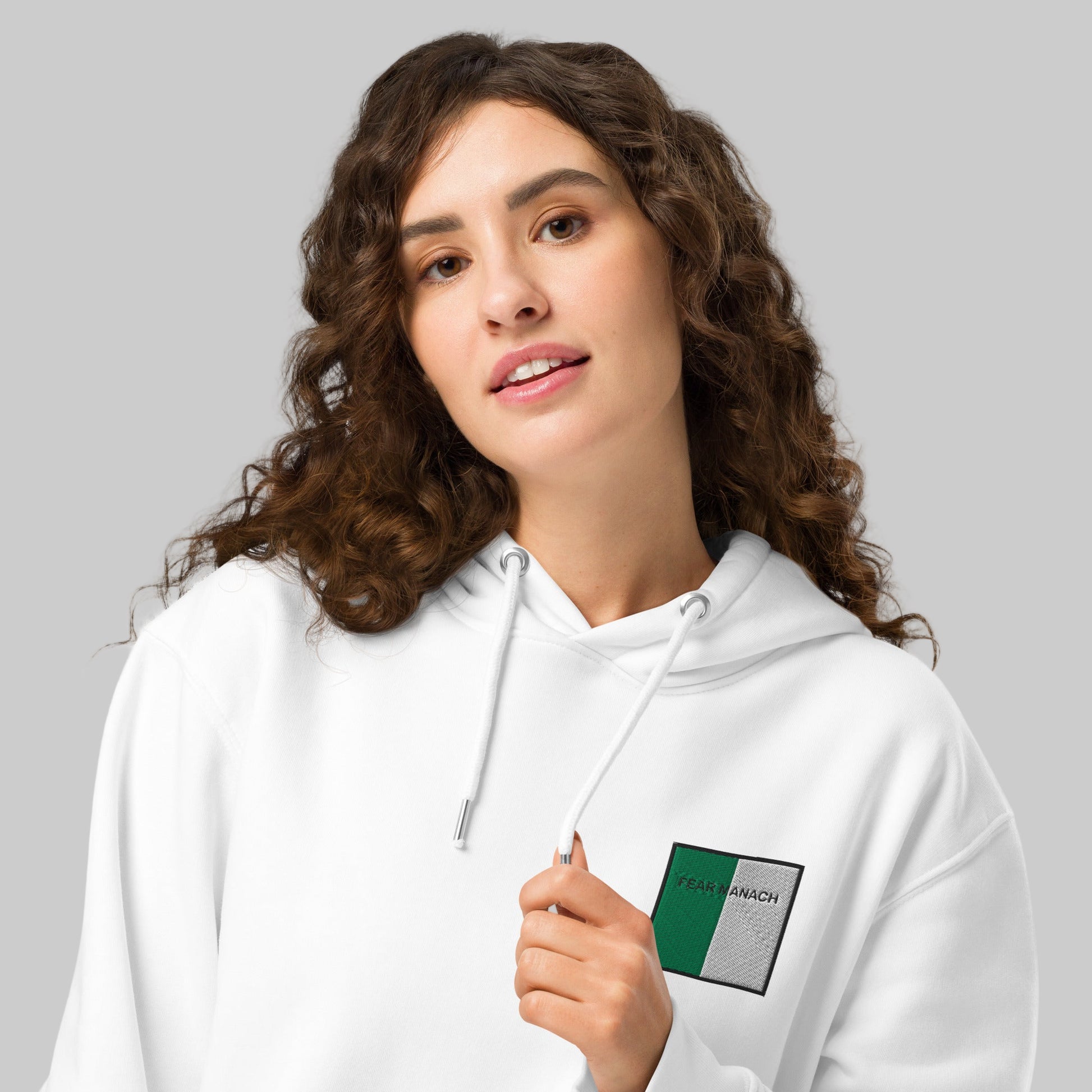 Woman wearing a white hoodie with a fear MANACH emblem front left