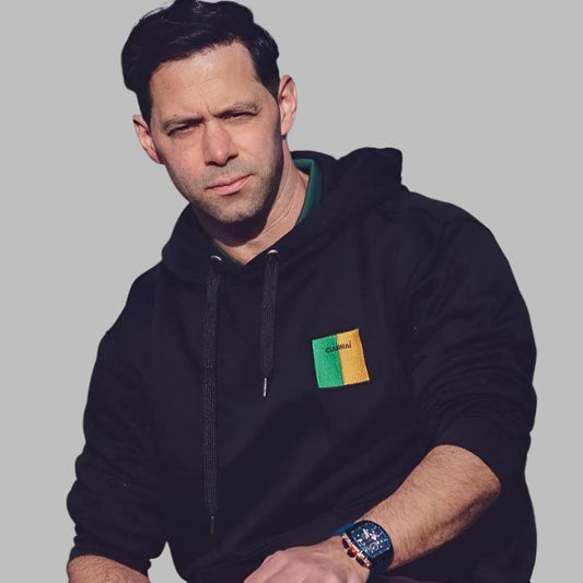 A man wearing a black unisex hoodie with an embroidered Ciarraí emblem on the front.