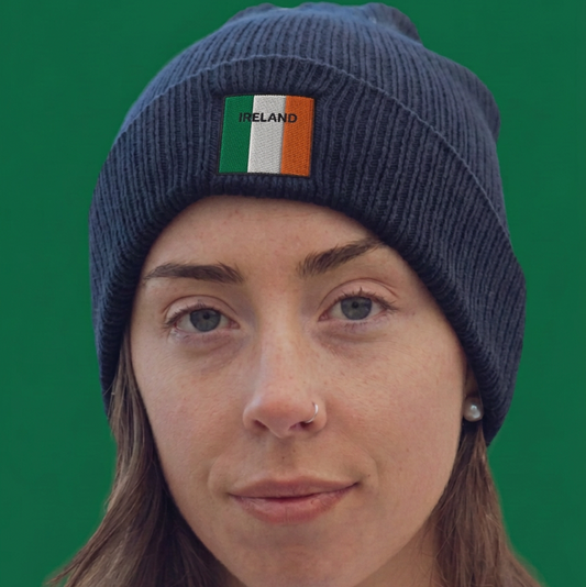 A woman wearing a navy blue ribbed knit beanie with an Irish flag patch on the front, set against a solid green background.