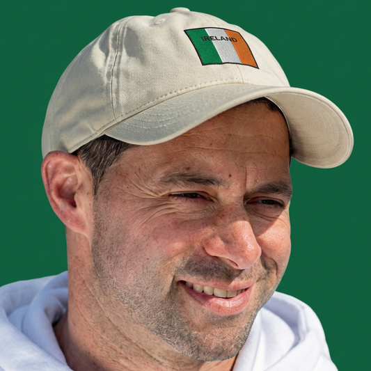 A man wearing a beige baseball cap with an Irish flag patch on the front, set against a solid green background.