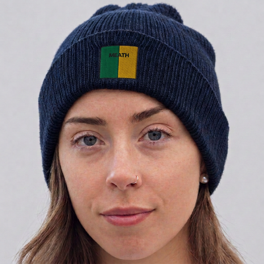 A close-up of a woman wearing a navy blue ribbed knit beanie with a small green and yellow square patch on the front that reads 'Meath '.