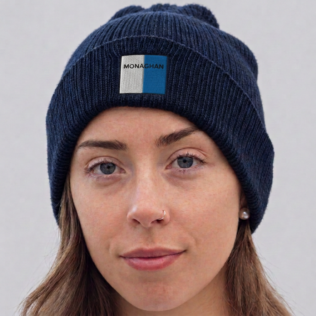 A close-up of a woman wearing a dark navy blue knit beanie with a pom-pom. The beanie features a front patch with the brand name 'MONAGHAN' printed on it.
