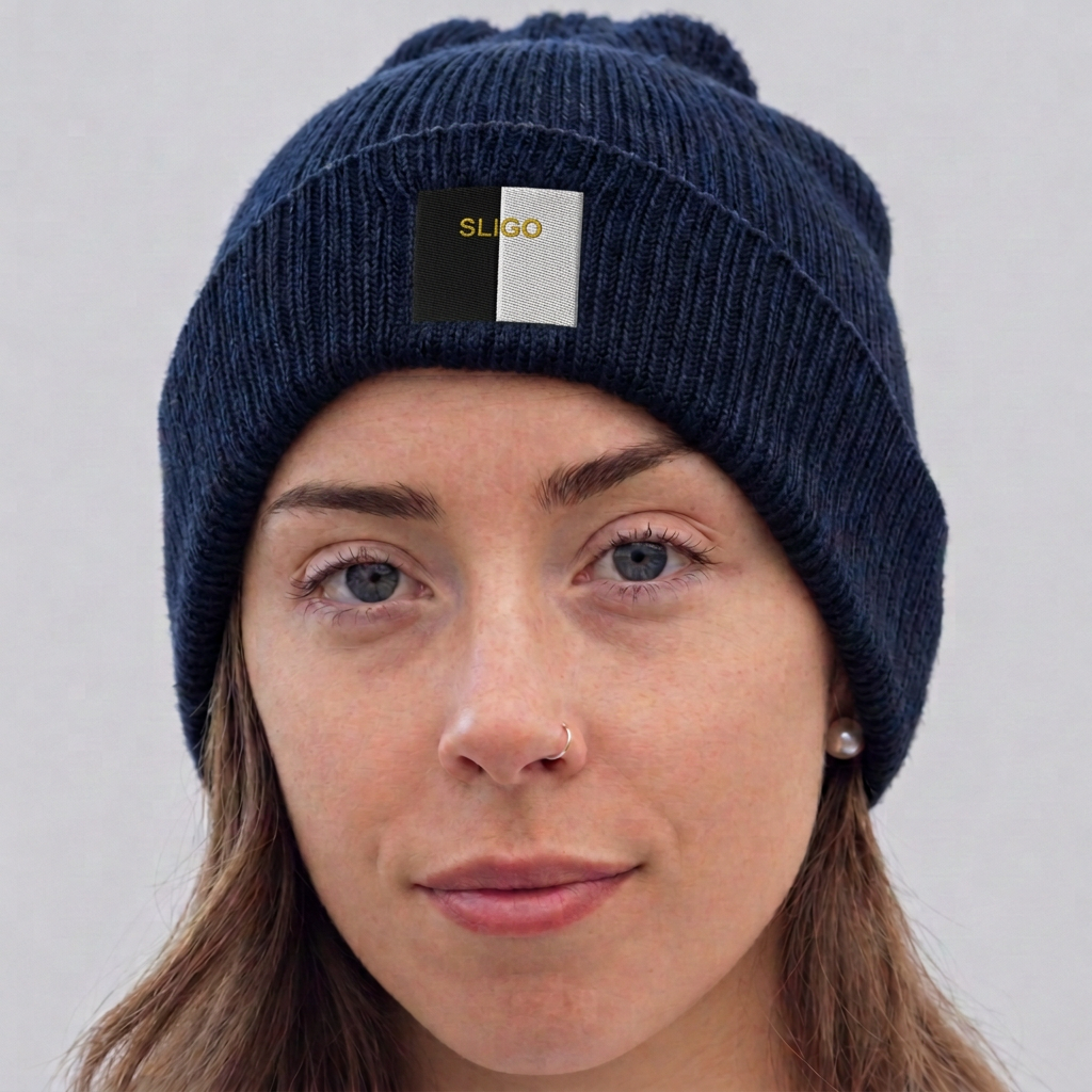A close-up of a woman wearing a dark navy ribbed knit beanie with a front patch that is split vertically into black and white, featuring the brand name 'SLIGO' in gold. The background is a clean, neutral light gray.