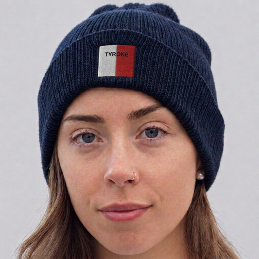 A close-up of a woman wearing a navy blue ribbed knit beanie with a small front patch that reads TYRONE in white text over a red and white square.